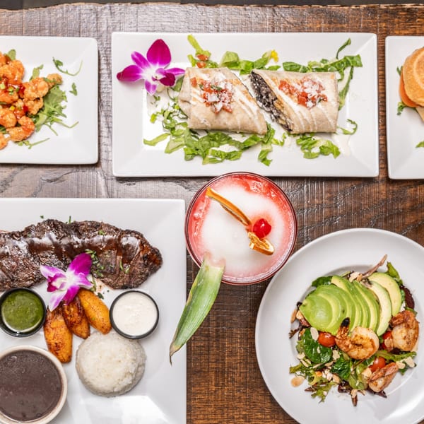A top-down view of various American dishes, including steak, shrimp, burritos, and a cocktail.