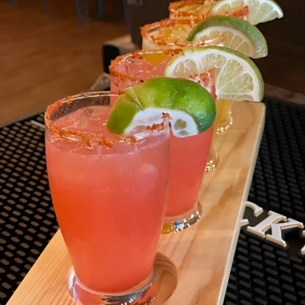Four colorful cocktails with lime wedges and chili-salted rims on a wooden tray at Catch 13 RVC.