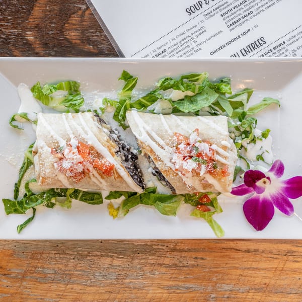 Two burritos with salsa, cheese, and crema on a bed of lettuce, garnished with an orchid.