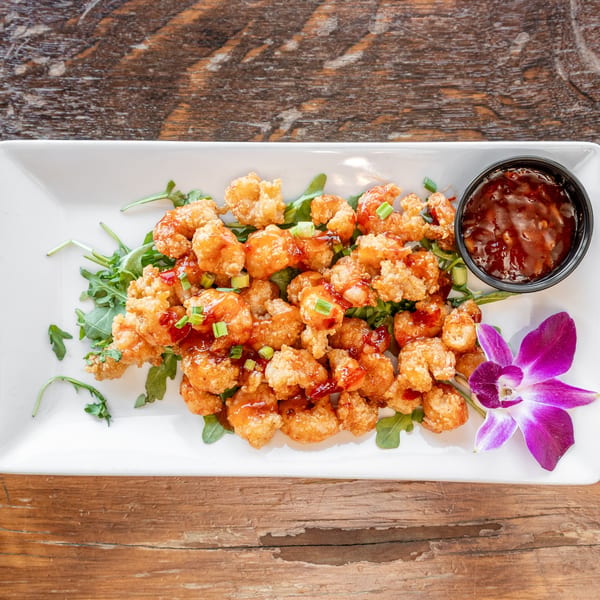 Crispy fried shrimp with sweet chili sauce, green onions, and a purple orchid on a white plate.
