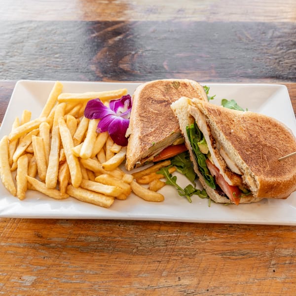 A Catch 13 RVC chicken sandwich with fries and a purple orchid on a white plate.